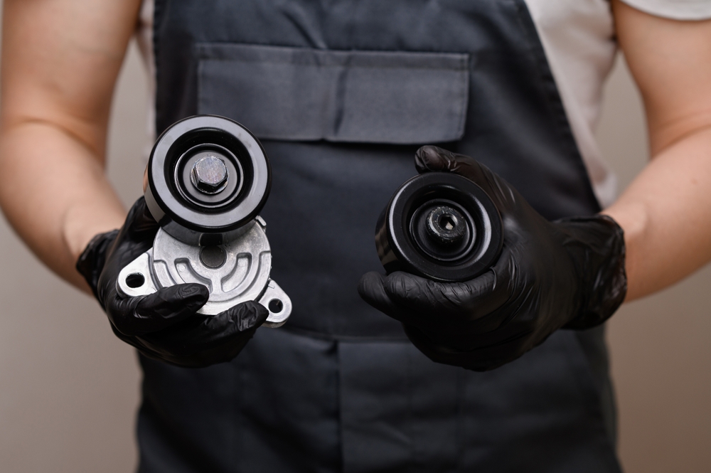 Auto mechanic holds in hands in black gloves tension roller with car serpentine belt tensioner and parasitic roller, close-up. Replacing auto parts, car maintenance, purchasing auto parts
