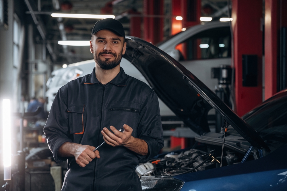 Front view, standing and holding tool. Mechanic working in a car service station.